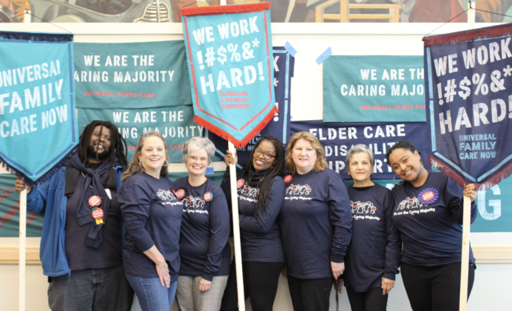 A group of seven women hold signs reading "We Work Hard!"